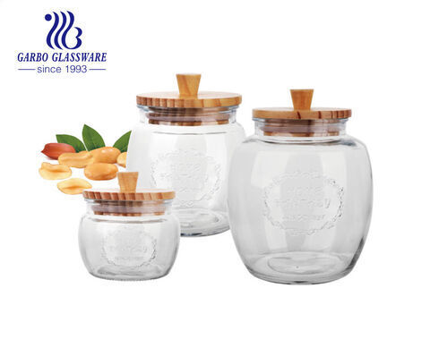 Venta al por mayor, botella de almacenamiento de vidrio barata hecha a máquina de varios tamaños, tarro de almacenamiento redondo con tapa de madera